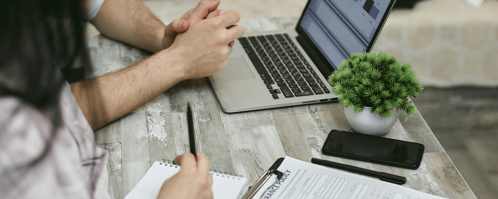 Close up of two people having a meeting with a laptop and notepad.